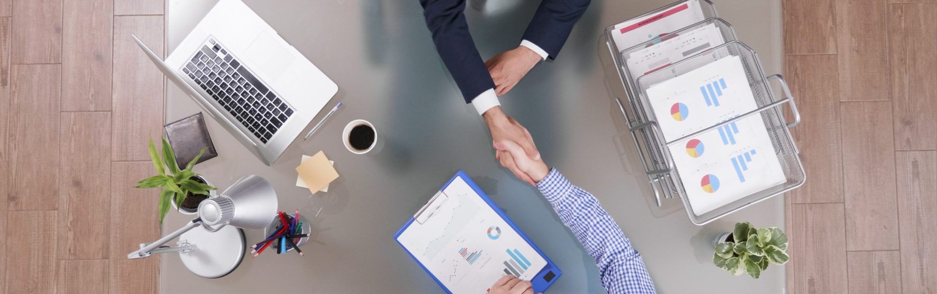 Top view of businessmen shaking hands during business negotiation in startup office discussing company strategy. Partners analyzing management profit planning investments meeting. Marketing documents